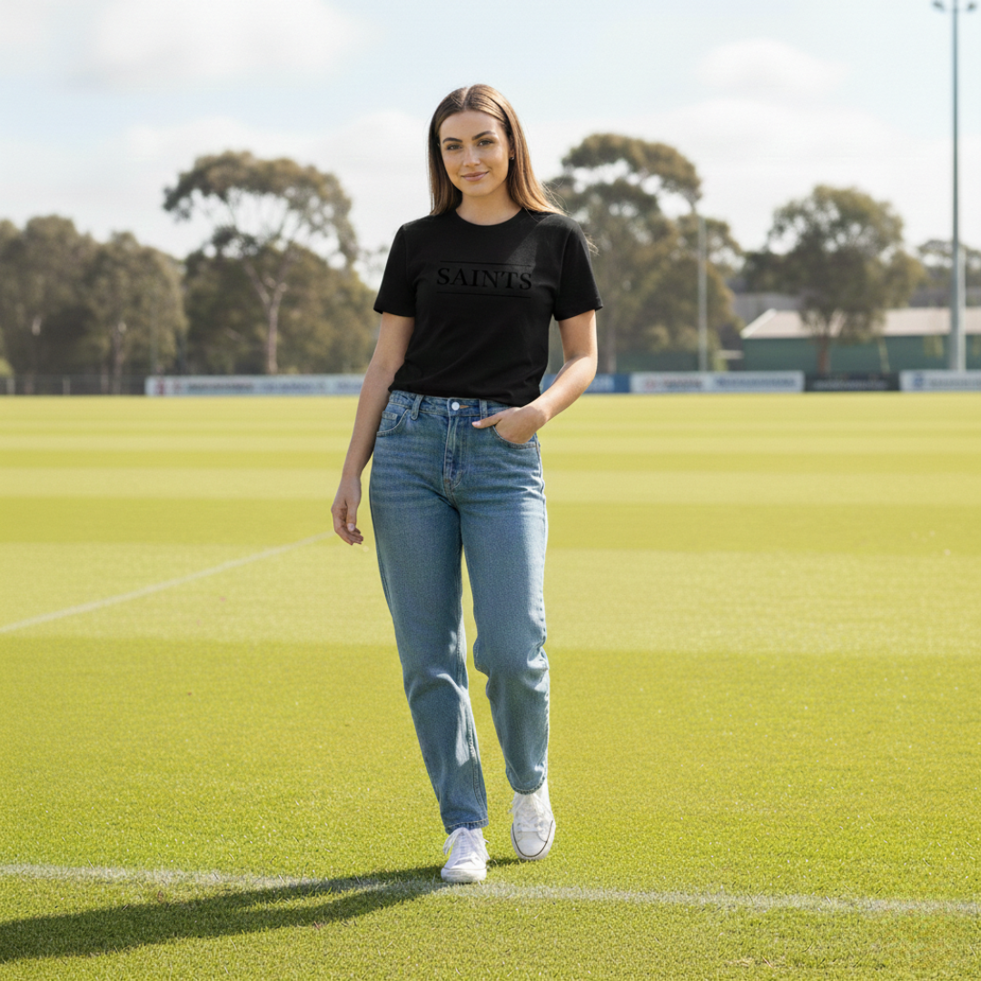 Woman in black t-shirt and blue jeans standing on a grassy field with trees in the background