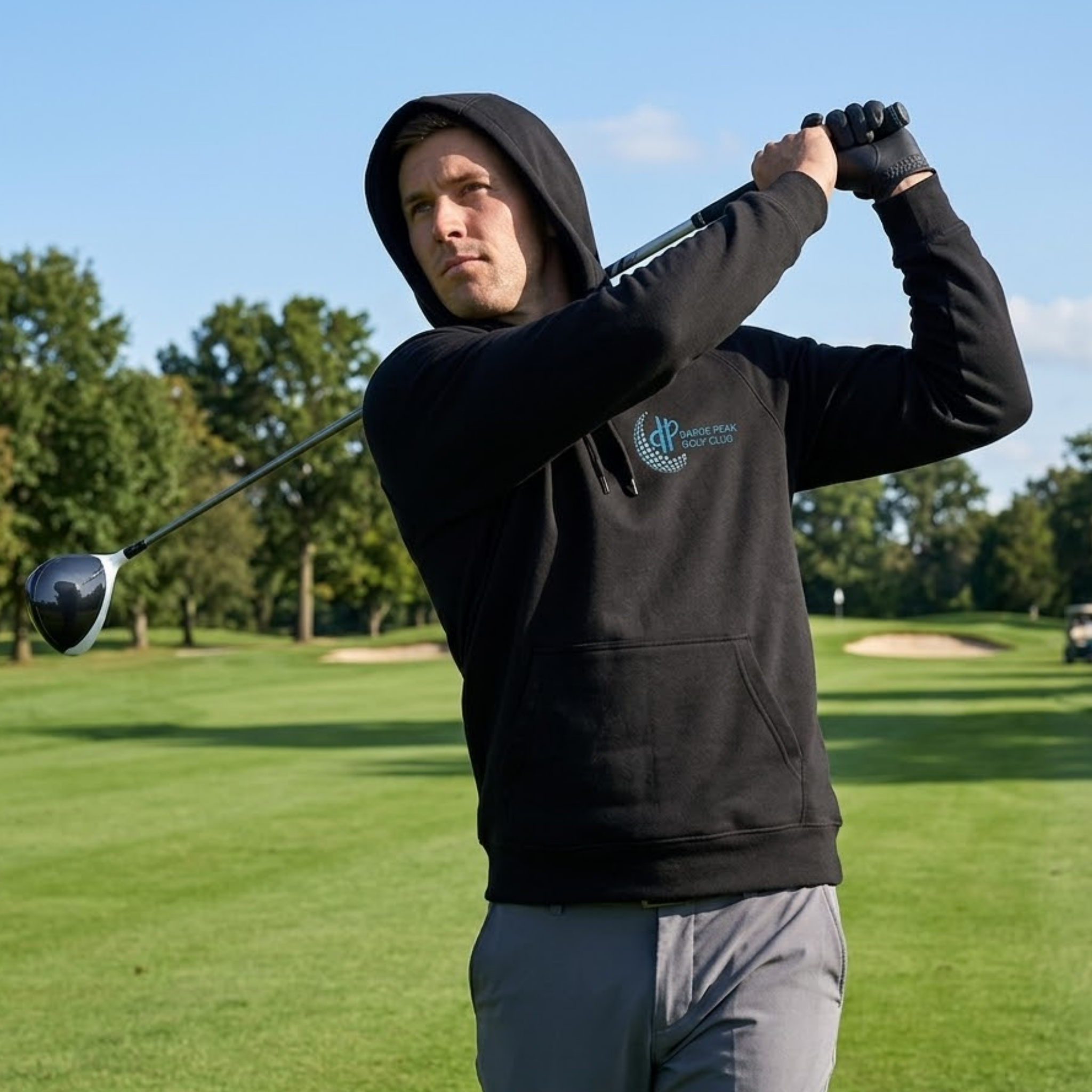 Man in a black hoodie swinging a golf club on a golf course