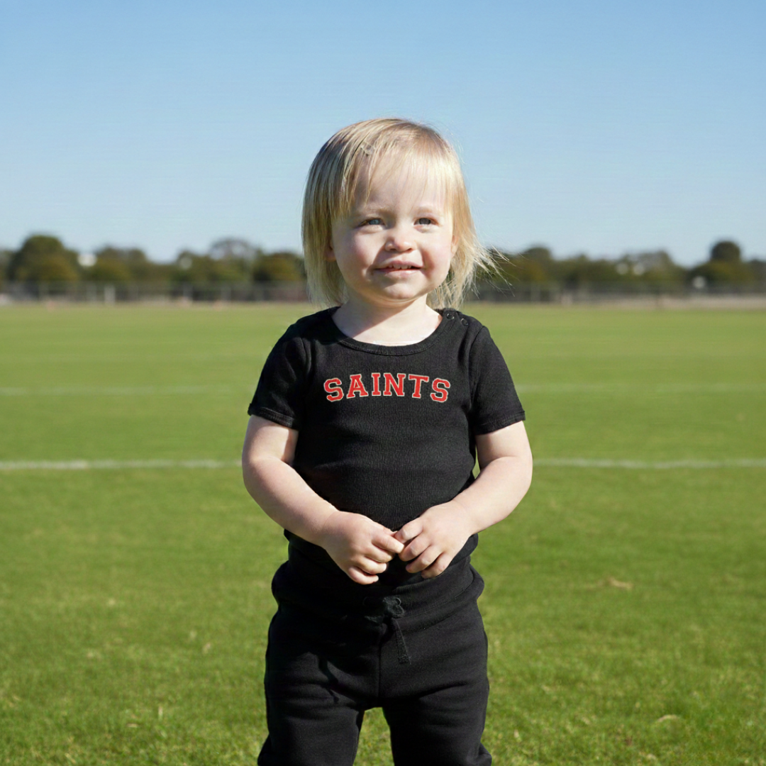 Toddler wearing SAINTS branded onesie on a football oval