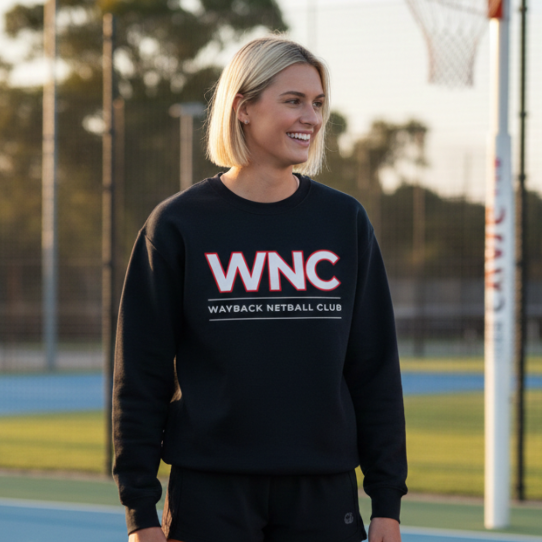 Woman wearing a navy sweatshirt with 'WNC Wayback Netball Club' on a sports field.