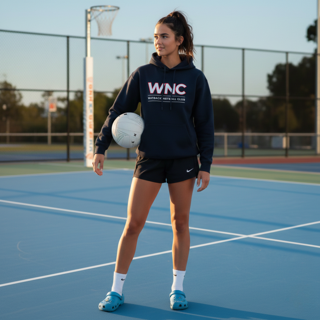 Woman holding a netball on a sports court wearing a hoodie with 'WNC' on it.