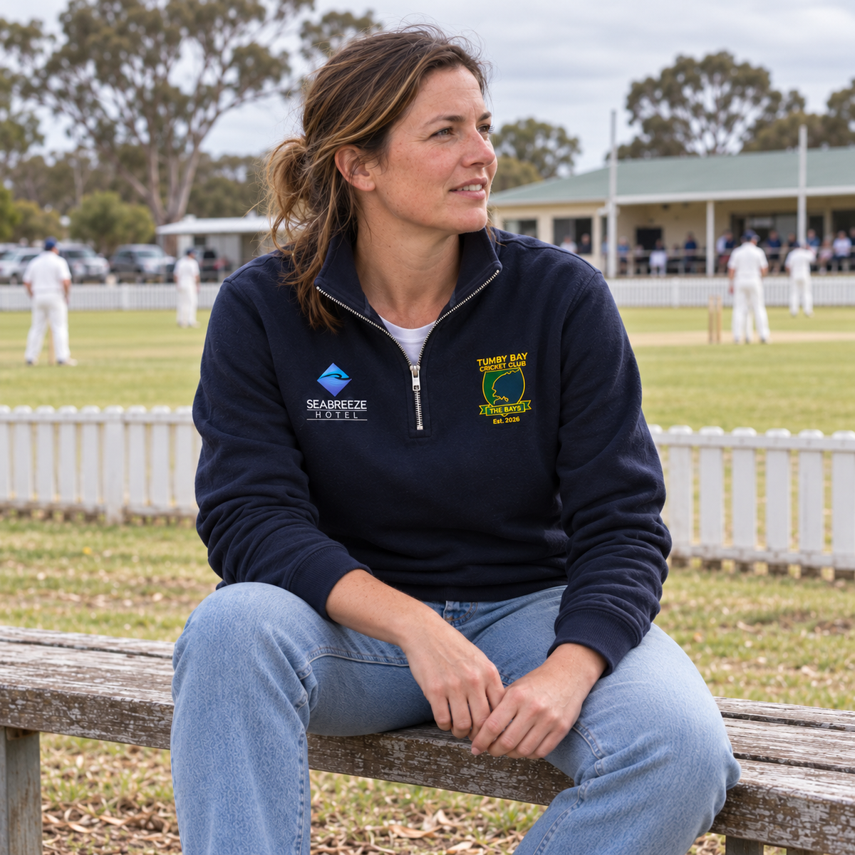 Woman wearing the Tumby Bay Cricket Club navy 1/4 zip on a bench at the cricket