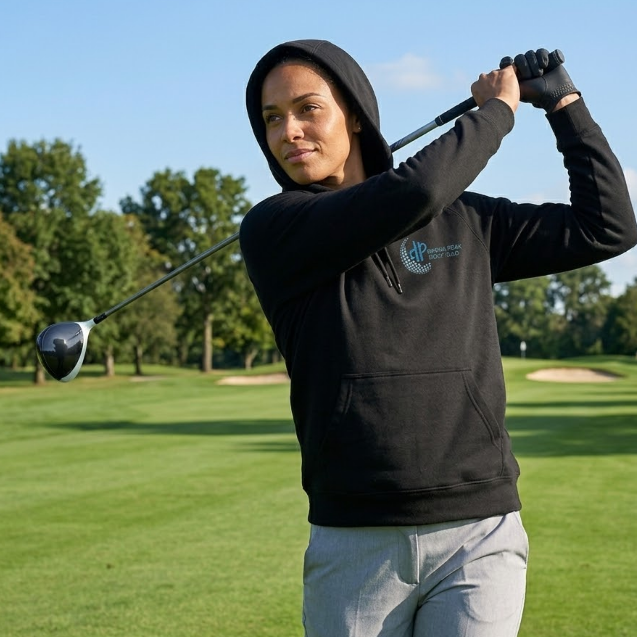 Person in a black hoodie with a logo holding a golf club on a golf course