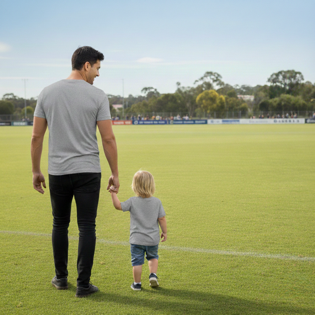 Man and child walking on a grassy field with trees and clear sky in the background