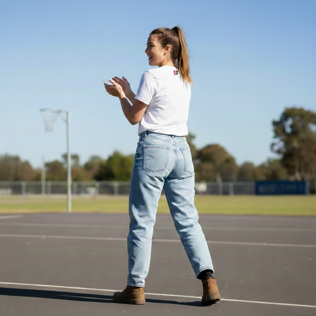 Woman standing on a sports field wearing a white t-shirt and light blue jeans.