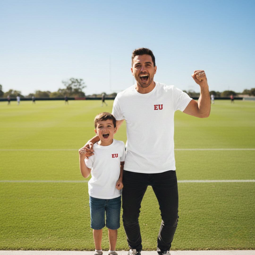 Man and child standing on a sports field wearing white shirts with 'EU' logo.