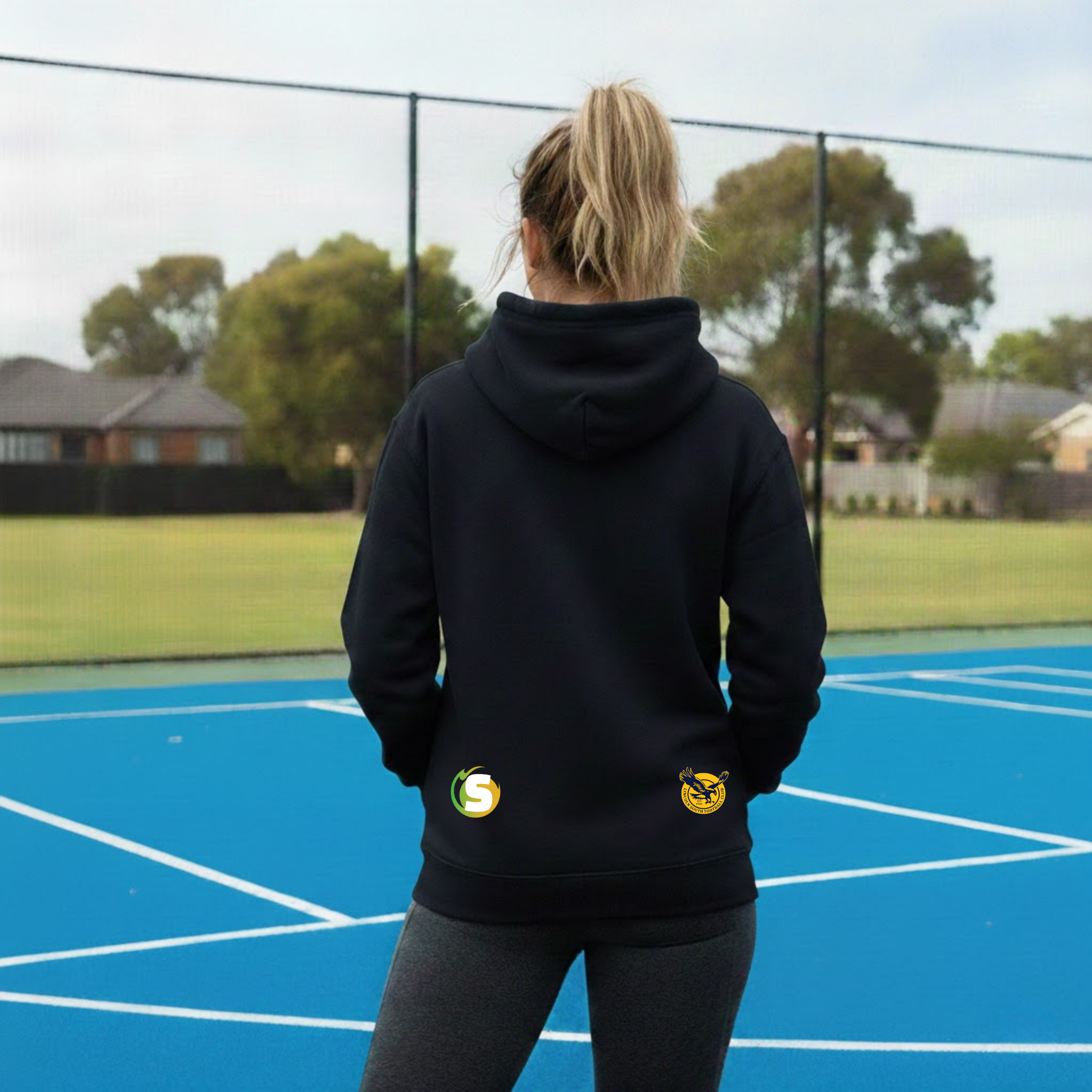 Person wearing a navy hoodie with logos on a blue sports court
