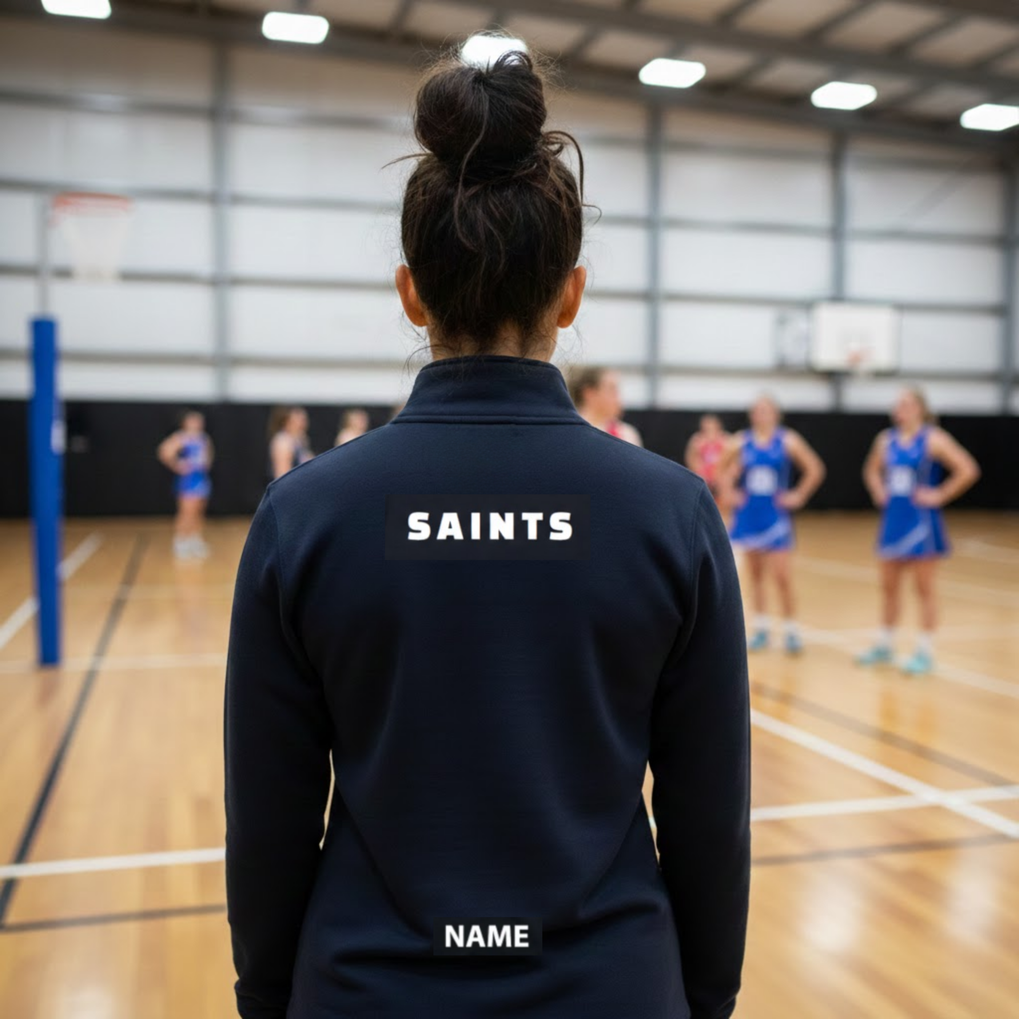 Person wearing a navy jacket with 'SAINTS' on the back, standing in a gymnasium with other people in blue uniforms.