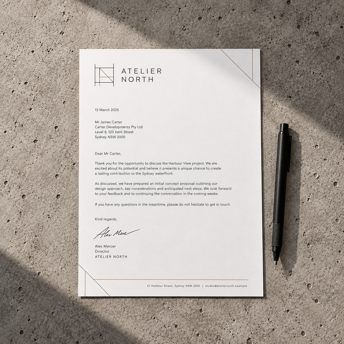 Minimal white Atelier North letterhead with charcoal text and fine copper lines, shown on a concrete surface beside a black pen.